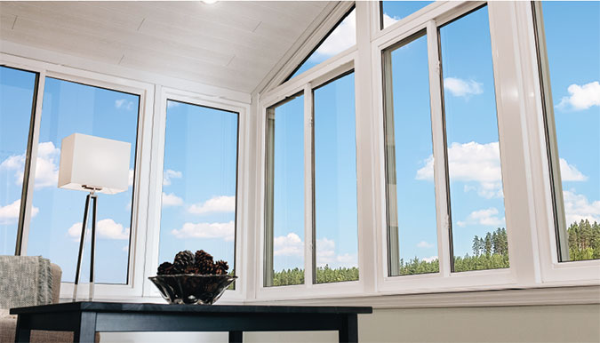 Interior view of a bright sunroom featuring large floor-to-ceiling windows, a cathedral-style ceiling, and scenic outdoor views.